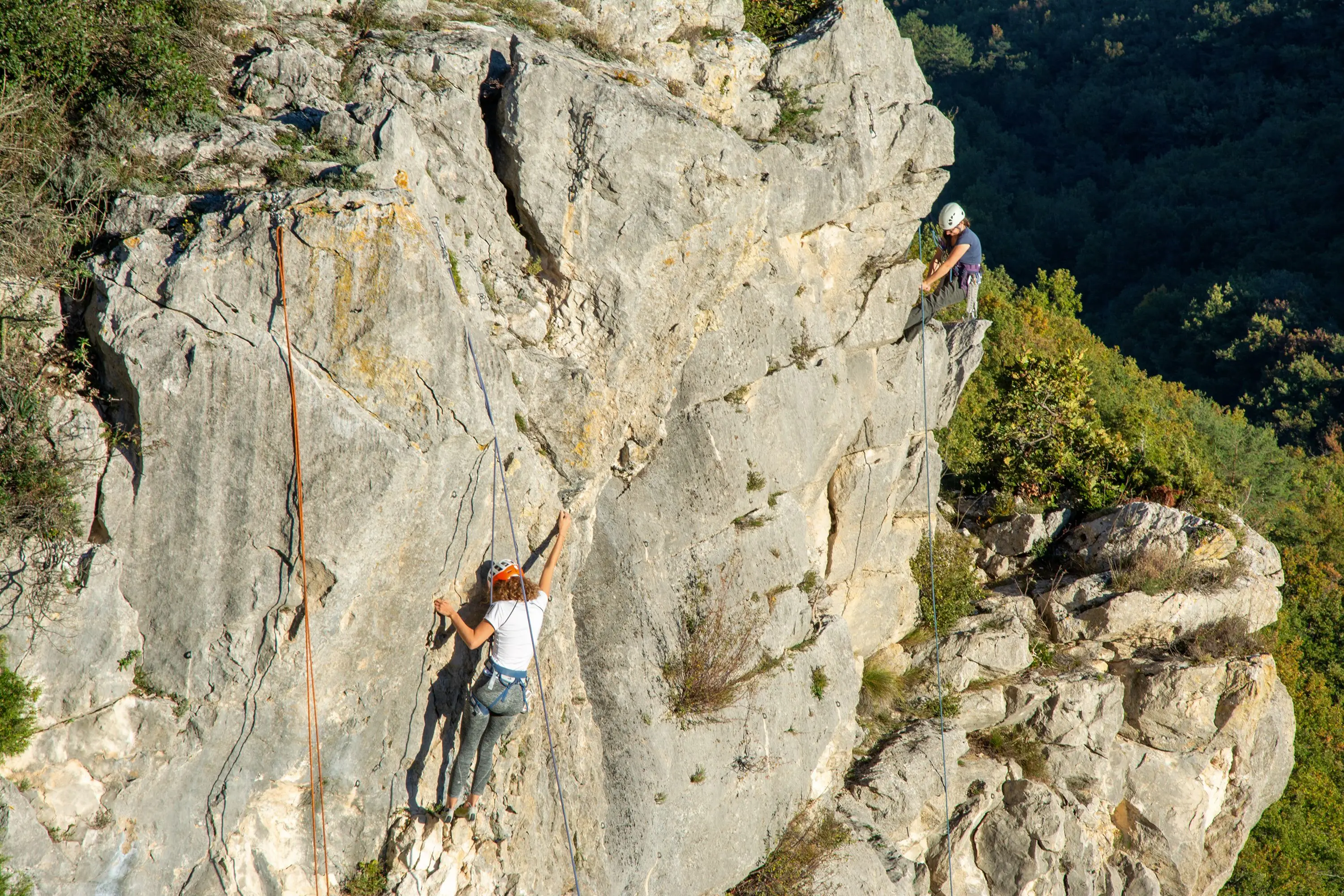 A climber on a rock face while her partner belays her from above