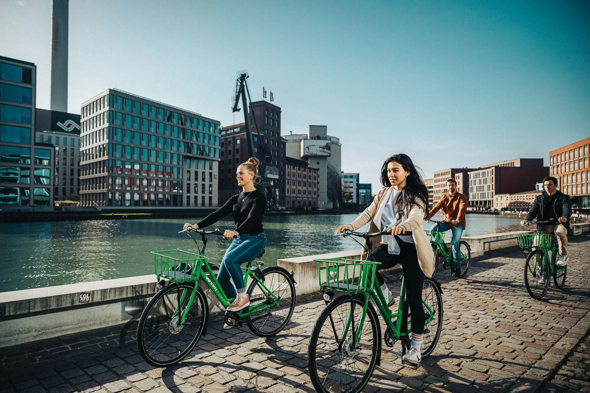 Four friends riding bikes together along a riverside path