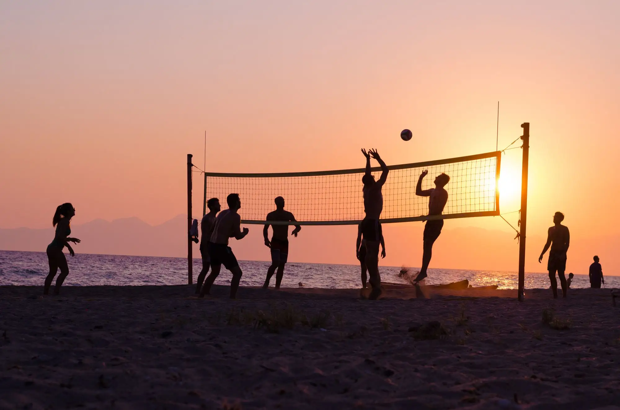 Silhouettes of people playing beach volleyball together at sunset